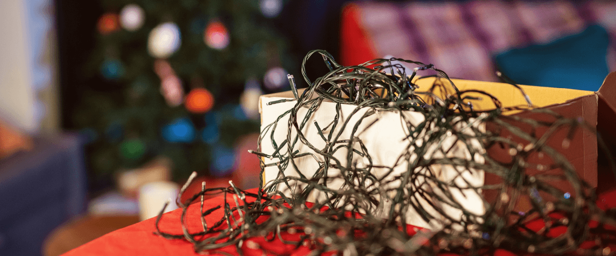 A box of tabgled christmas lights on a red table. A Christmas tree is in the background